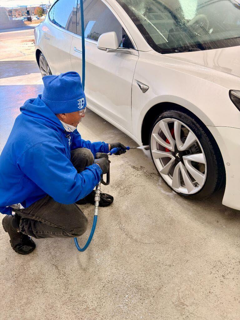 Brightworks Fort Worth team member crouching to pressure-rinse the Tesla Model 3 wheels with a precision water gun